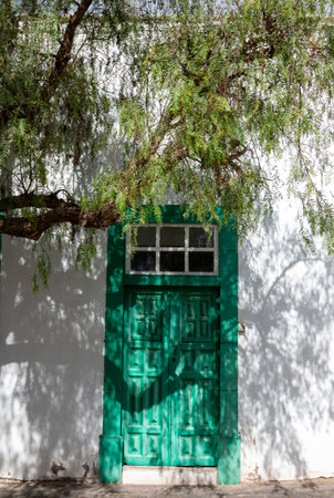 White architecture, typical for the island. Green doors and windows. Respect to the nature, old trees between the buildings. Blue sky with white clouds. Teguise, Lanzarote, Canary Islands, Spain.の写真素材