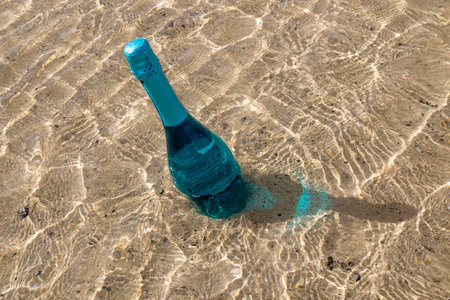 Bottle with unusual turquoise sparkling wine in the shallow water on the beach, enlighted by sunlight. Lanzarote, Canary Islands, Spain.の写真素材