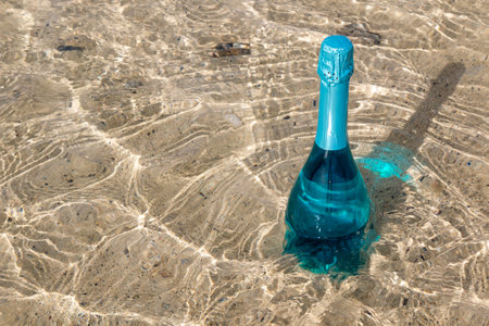 Bottle with unusual turquoise sparkling wine in the shallow water on the beach, enlighted by sunlight. Lanzarote, Canary Islands, Spain.の写真素材