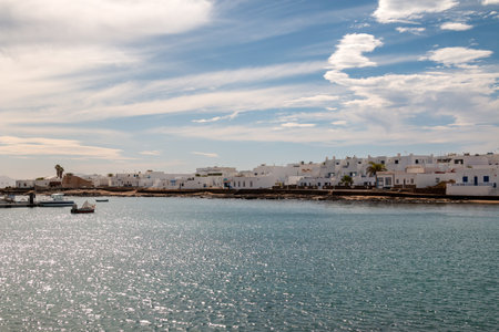 View on the island La Graciosa from a boat. Calm water of Atlantic ocean and a typical white architecture. Blue sky with white clouds in the winter. Caleta del Sebo, La Graciosa, Canary Islands, Spain.の写真素材