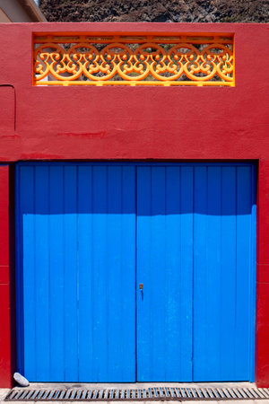 Multicolored house in a bright sunshine. Bright blue gate, red wall and dark yellow railing on the terrace. Madalena do Mar, Madeira, Portugal.の写真素材