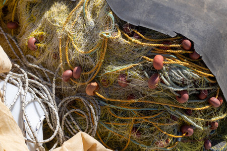 Yellow fishing nets in a pile on the coast in the port. Orange round buoys. Sunny summer day....