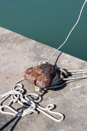 Old rusted bollard on the coast of a marina. White rope. Diagonal line of the Ionic sea, bright green color. Port in Astrakeri, Corfu, Greece.の写真素材
