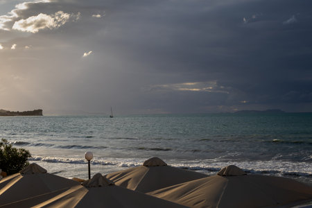 Top of the sun umbrellas in a restaurant. Ionic sea with waves during a stormy late summer day. Boat on the sea. Cloudy dark sky. Acharavi, Corfu, Greece.の写真素材