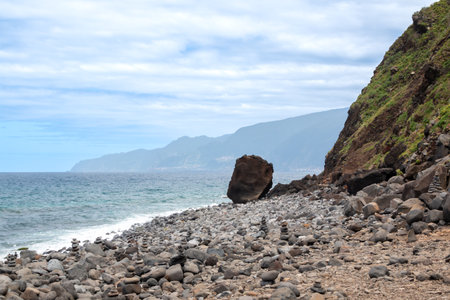 Volcanic rock, creating high cliff on the coast of the Atlantic ocean on the North of the island. Calm turquoise water and blue sky with white clouds. Ribeira da Janela, Madeira, Portugal.の写真素材