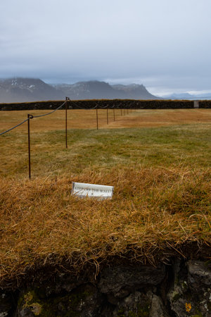 Notice on a small wall, covered by autumn grass "Keep off the wall" - the land is a part of cemetery. Mountains in the background. Cloudy rainy sky. Budhir, west Iceland.の写真素材
