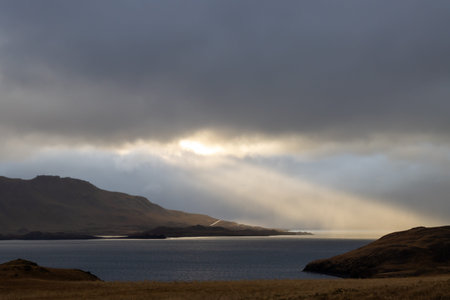 Calm water of fjord Hvalfjordur, surrounded by mountains. Cloudy sky with a wide ray of sunshine....