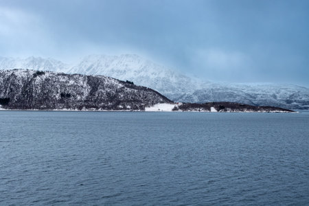 Snow-covered landscape. Mountains and a water of a Kvaerfjord. Colorful cloudy sky during...