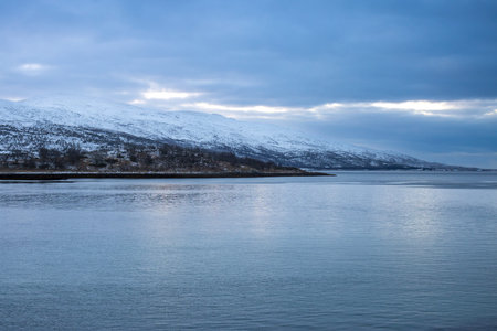 Coast of the Norwegian sea in blue tones of a winter short day.. Mountains in the background. Land covered by snow. Cloudy sky in the late autumn. Kongsvika, Norway.の写真素材