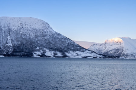 Mountains lined by calm water of the Norwegian sea. Colorful clouds in the surise/sunset of a short arctic day. Grovfjord, Norway.の写真素材