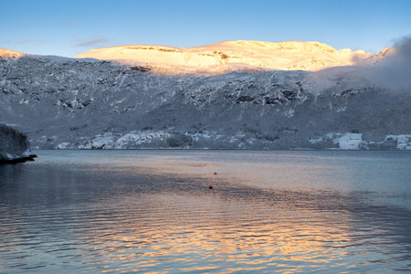 Majestic mountains covered by snow, lining the calm water of a fjord (Norwegian sea). Sunshine and a...