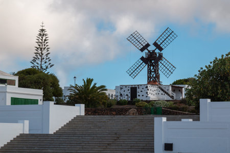 Windmill as a part of a park with various greenery and large staircase. Blue sky with white clouds....