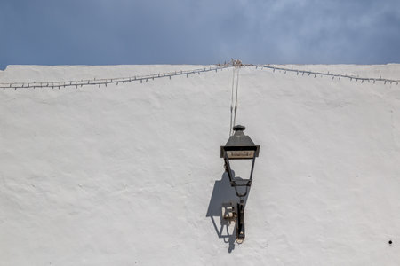 White wall with a traditional lantern. Cable with small lights. Everything with its shadow. Blue sky with white clouds. Teguise, Lanzarote, Canary Islands, Spain.の写真素材