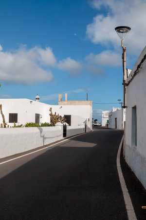 Asphalt road lined by traditional white houses. Street lamp. Curve of the road. Blue sky with white clouds, Lanzarote, Canary Islands, Spain.の写真素材