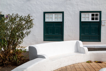 Square with a park and built white bench and a wall of flower bed. White facade in the background with two dark green windows. Teguise, Lanzarote, Canary Islands, Spain.の写真素材
