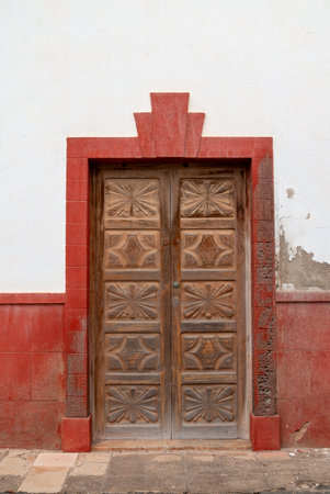 Old ornated wooden door with a red frame as a part of decoration on the white facade. Street in Teguise, Lanzarote, Canary Islands, Spain.の写真素材