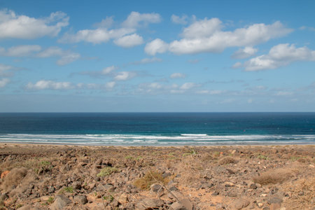 Volcanic rocks on the coast of the Atlantic ocean. Beach with a white sand. Cloudy sky. Famara,...