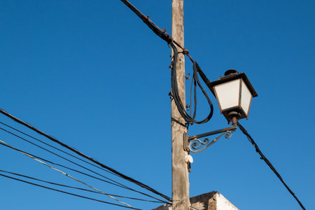 Classical style of a street lantern on a weathered wooden pole. Many cables. Bright blue sky. Lanzarote, Canary Islands, Spain.の写真素材
