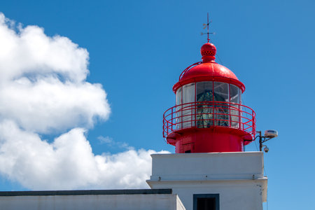 Building of a lighthouse with white facade and red tower. Located on a top of a cliff. Blue sky with light white clouds. Ponta do Pargo, Madeira, Portugal.の写真素材