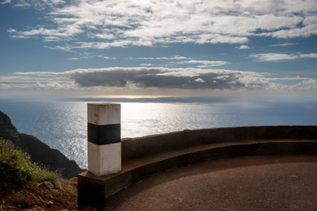View from a cliff on the Atlantic ocean, glossy in the evening sunlight. Blue sky with white clouds. Santa Maria Madalena, Madeira, Portugal.の写真素材