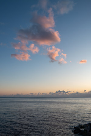 Stones as a part of a pier. Calm Atlantic ocean during a sunset.  Pink clouds on the sky. Ponta do Sol, Madeira, Portugal.の写真素材