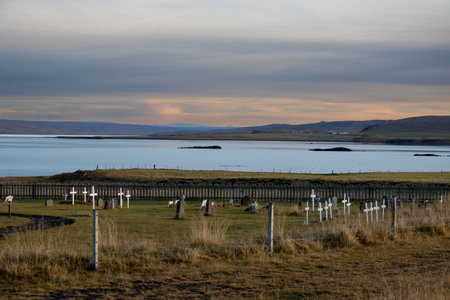 Small cemetery beside a fjord of Atlantic ocean. Green grass and crosses. Mountains in the background. Evening cloudy sky. North of Iceland.の写真素材