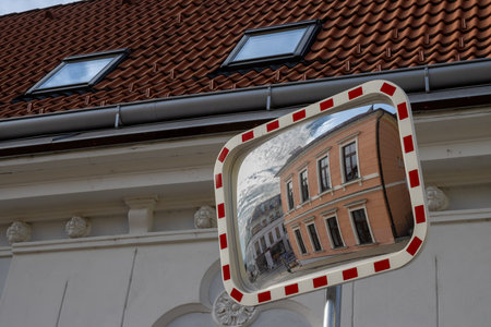 Traffic mirror with white-red frame, reflecting a classic house with an orange facade and blue sky...
