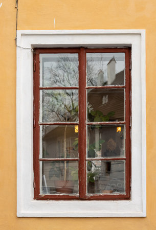 Yellow facade of a house in the historical city centre. Window with a white frame and lights inside....
