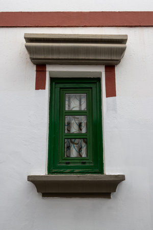 Small window with a green frame and red details on the white facade of the house. Puerto de Mogan,...
