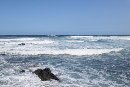 Big volcanic black rocks on the coast of Atlantic ocean with intense waves during winter windy day. Blue sky with white clouds. Las Palmas, Gran Canaria, Canary Islands, Spain.の写真素材