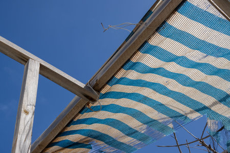 Wooden construction on a roof af an abandoned house. Broken blue and white striped textile shade and...