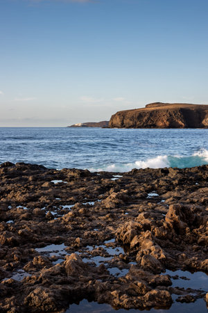 Rocky coast of Atlantic ocean. Waves during a windy winter day. Mountain in the background. Blue sky...