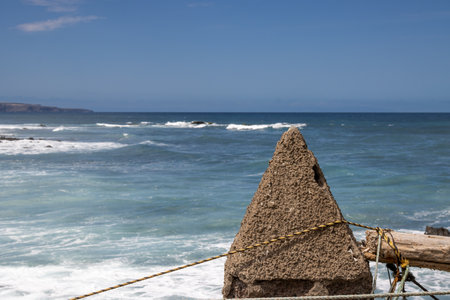 Pyramide shape of a concrete object, used to fix boats or fishing nets. Coast of Atlantic ocean with a mountain in the background. Quintanilla, Las Palmas, Gran Canaria, Canary Islands, Spain.の写真素材