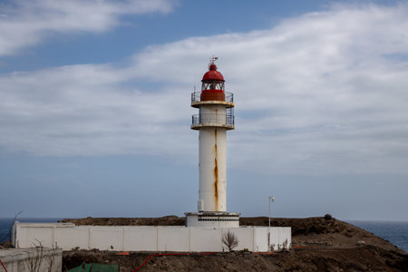 Lighthouse with white facade and red top, traditional style. Blue sky with intense clouds. Coast of...