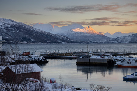 Small port on a calm Norwegian sea. Nature covered by snow. Mountains in the background. Colorful...
