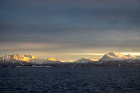 Calm water of sea. Mountains covered by snow, bright yellow color in the arctic sunrise. Colorful...