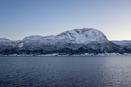 Calm water of the Norwegian sea. Nature and high mountains in the background, everything covered by...