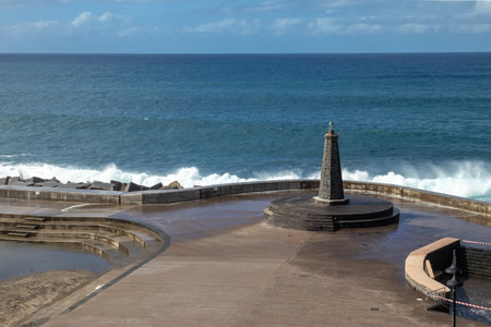 Town beach with a lighthouse. Big waves of Atlantic ocean in the autumn. Blue sky with white clouds. Bajamar, Santa Cruz, Tenerife, Spain.の写真素材