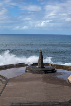 Town beach with a lighthouse. Big waves of Atlantic ocean in the autumn. Blue sky with white clouds. Bajamar, Santa Cruz, Tenerife, Spain.の写真素材