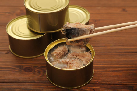 Open tin can with fish and chopsticks on wooden table, closeupの写真素材