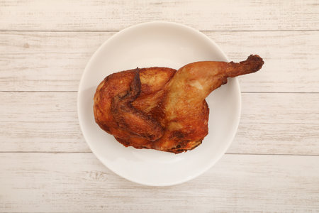 Fried half a chicken on a white plate on a white wooden background.の写真素材