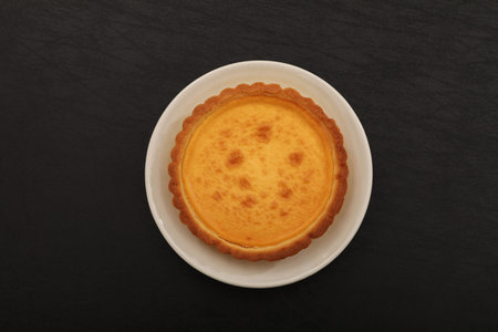 Cheesecake tart on a white plate on a black background, top viewの写真素材