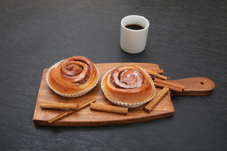 Cinnamon rolls with a cup of coffee on a wooden board.の写真素材