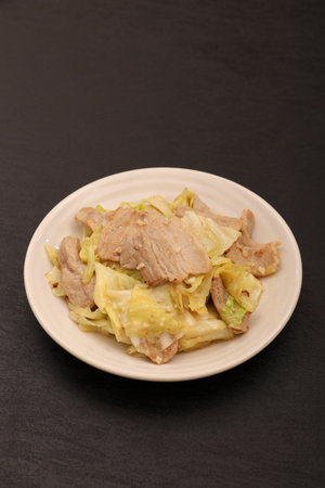 Stir-fried  cabbage with pork in a white plate on a black backgroundの写真素材