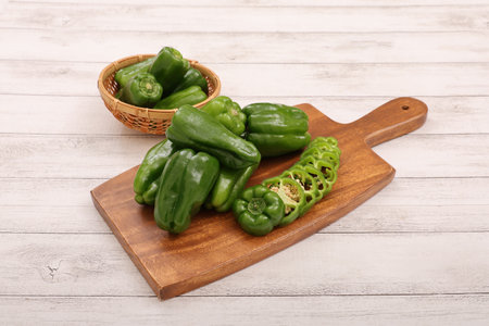 Green bell peppers on a cutting board, on a white wooden backgroundの写真素材