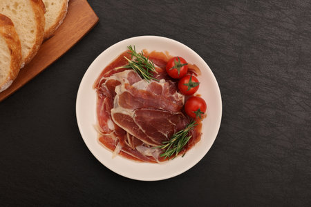Italian prosciutto crudo or jamon with rosemary and tomatoes on black backgroundの写真素材