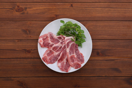 Raw pork chops on a white plate on wooden background. Top viewの写真素材