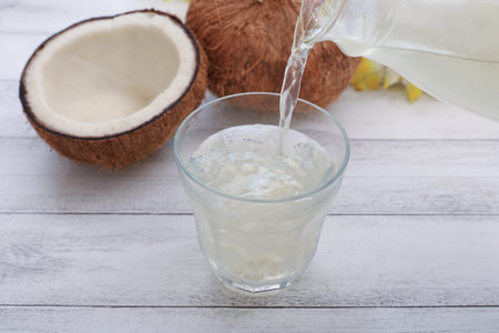 Coconut juice pouring into glass on wooden background, close upの写真素材