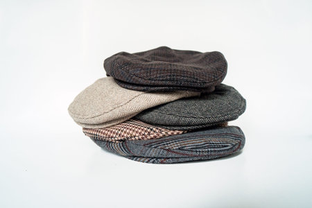 Stacks of classic hats like newsboy hats and flat hats in different colors and designs on a white...