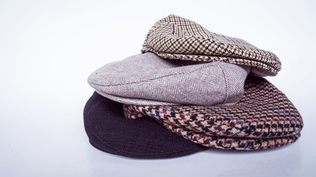 Stacks of classic hats like newsboy hats and flat hats in different colors and designs on a white...